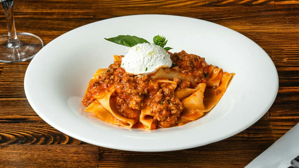Wide pasta with rich bolognese, creamy cheese, and fresh basil.