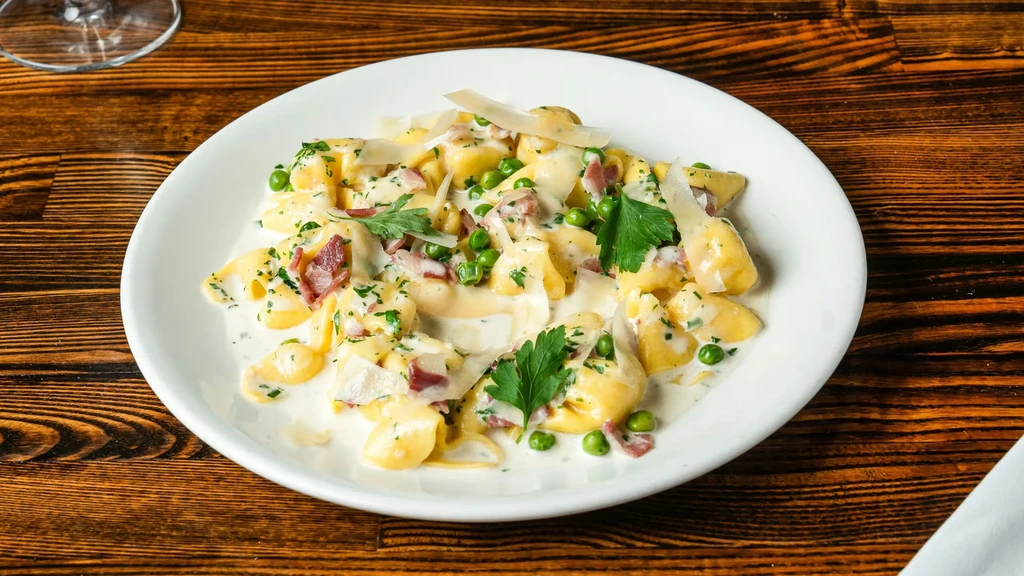 Plate of creamy pasta with peas, bacon, herbs, and Parmesan.