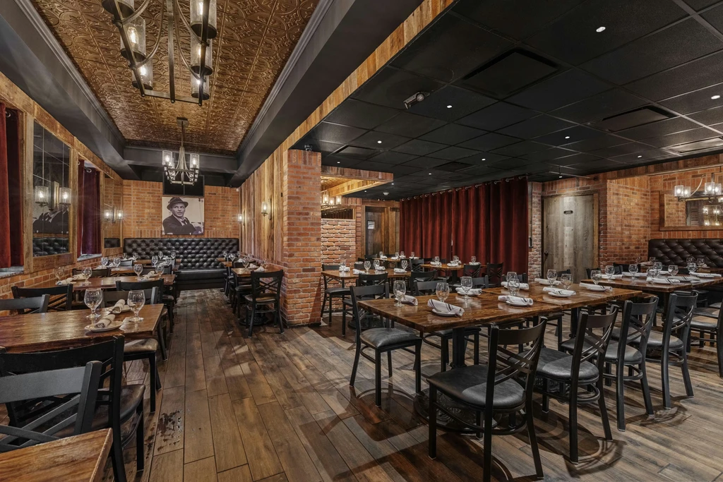 Empty restaurant: exposed brick, dark wood, set tables, warm lighting.