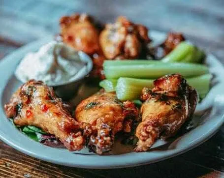 A plate of chicken wings with celery sticks and a small bowl of dip.
