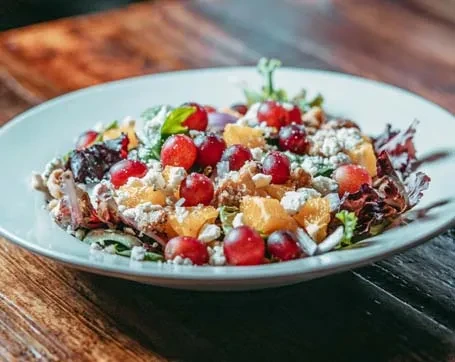 Mixed green salad with grapes, feta cheese, and oranges on a white plate.