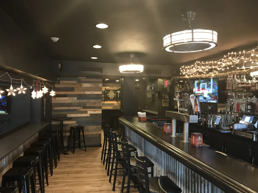 A dimly lit bar with a long bar, stools, and a dartboard.