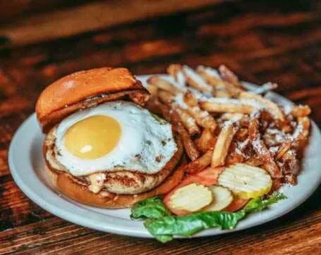 A burger with a fried egg and fries, garnished with pickles and lettuce.