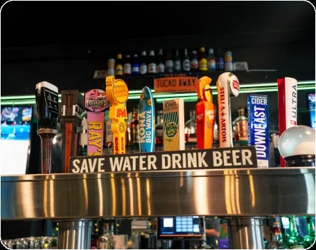 A row of beer taps with various brand handles and a "SAVE WATER DRINK BEER" sign.