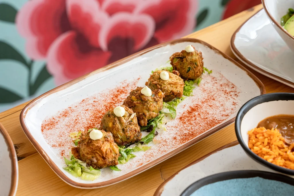 Five deep-fried fritters on a bed of lettuce with a dollop of sauce.