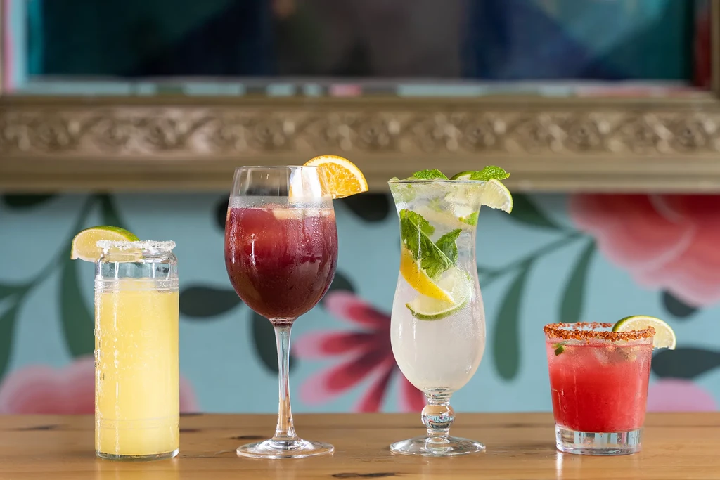 Four mixed drinks with garnishes sit on a wooden bar.