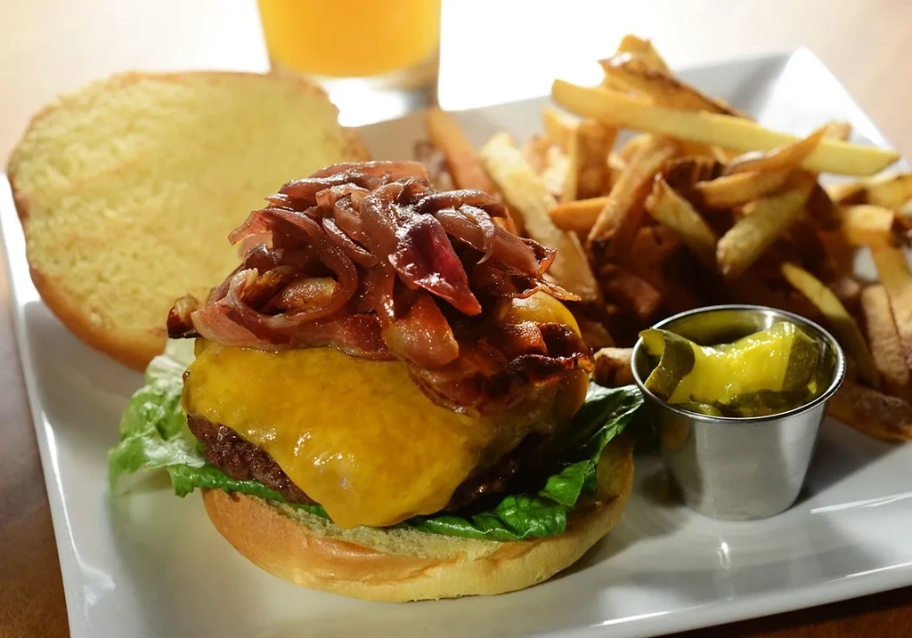 Cheeseburger with caramelized onions, fries, and pickles on a white plate.