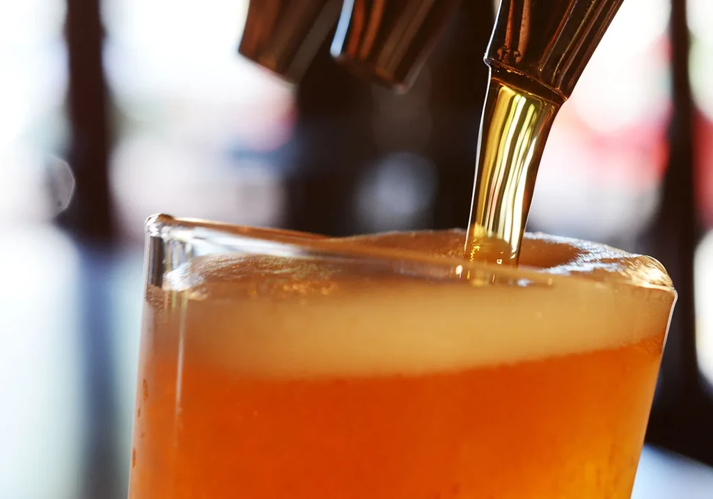 Beer pouring from a tap into a glass, creating a foam head.