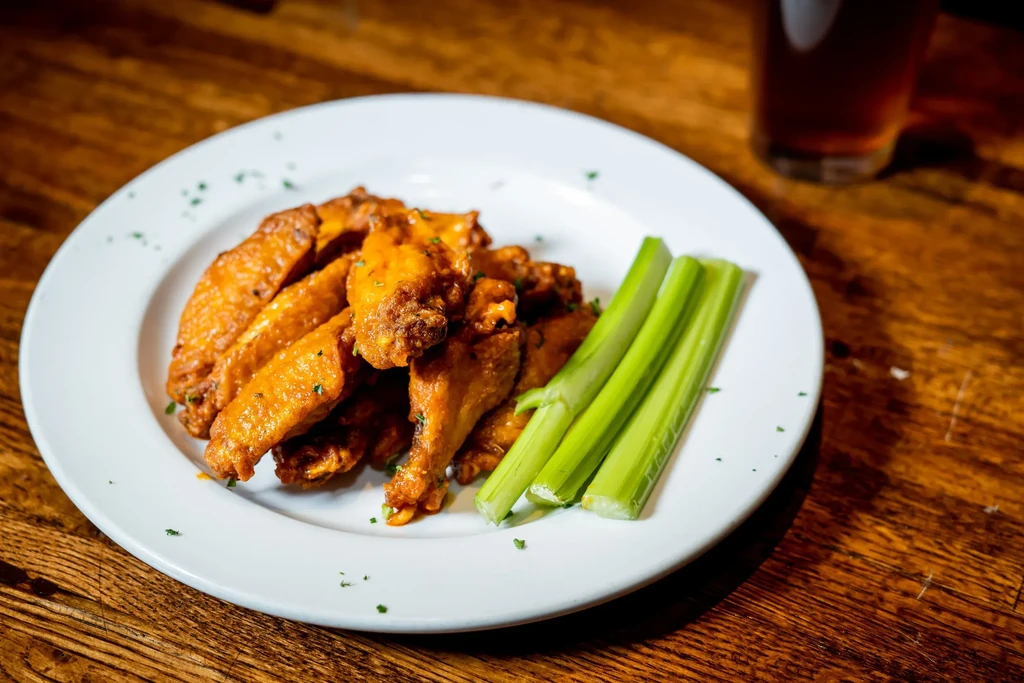 A plate of chicken wings with celery sticks and a drink.
