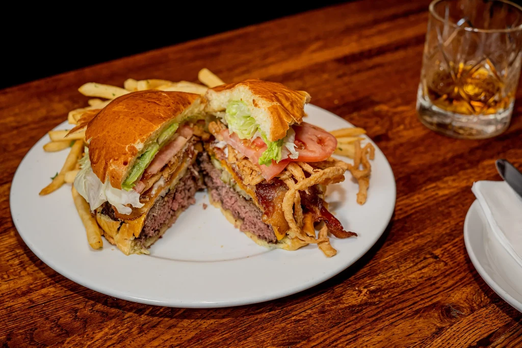 A burger cut in half with fries, bacon, lettuce, and tomatoes.