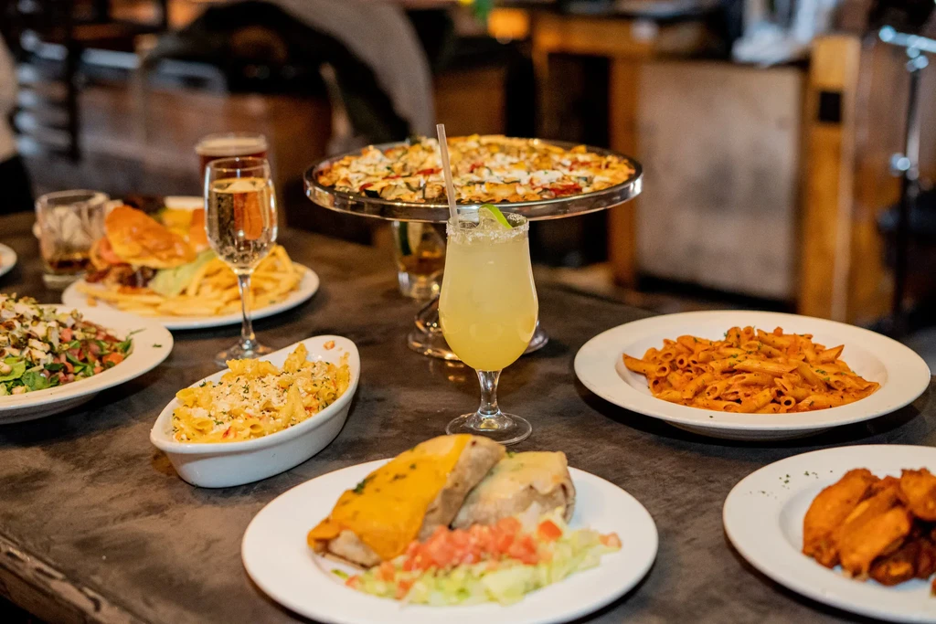 A table filled with various dishes, drinks, and a pizza on a stand.