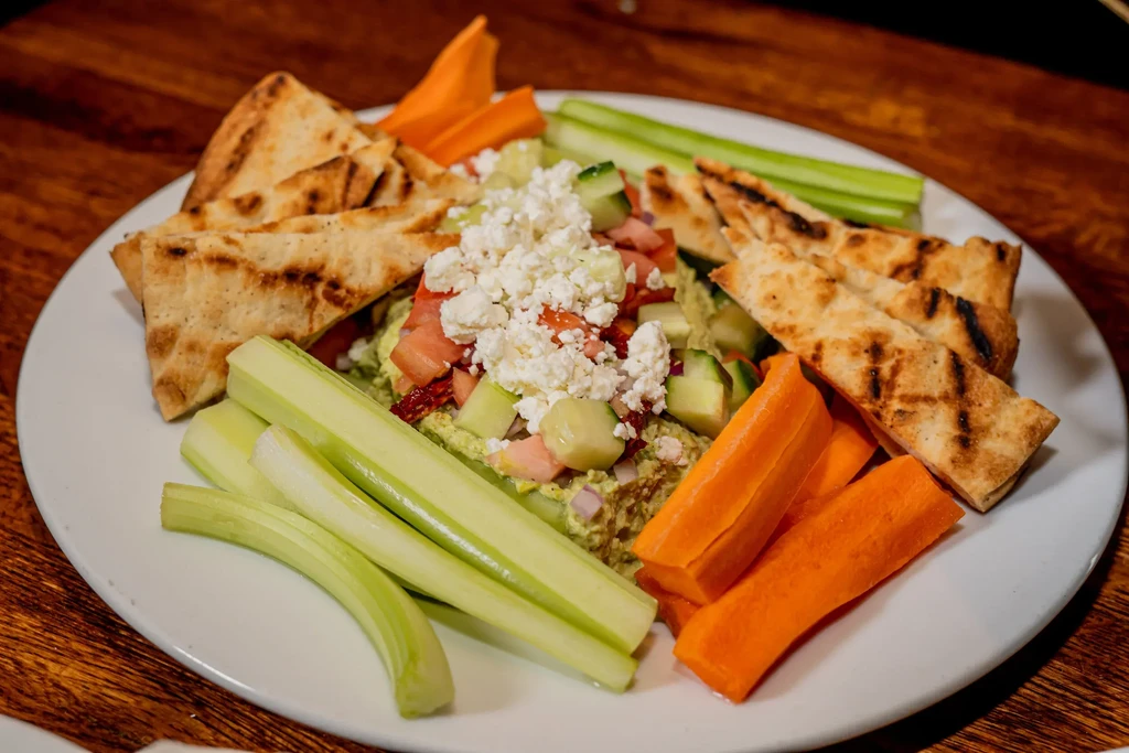 A plate of hummus with pita bread, celery, and carrots.