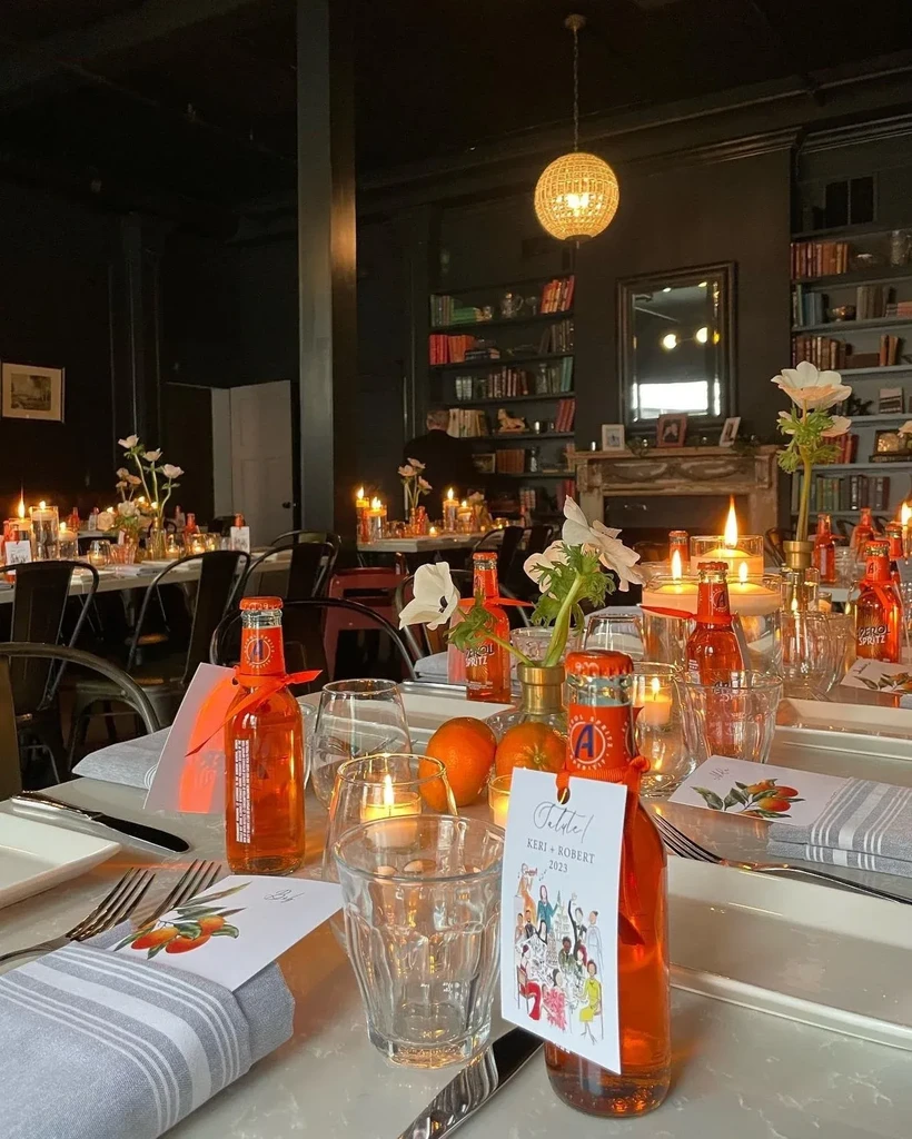 Tables set for an event with orange drinks, candles, and flowers.