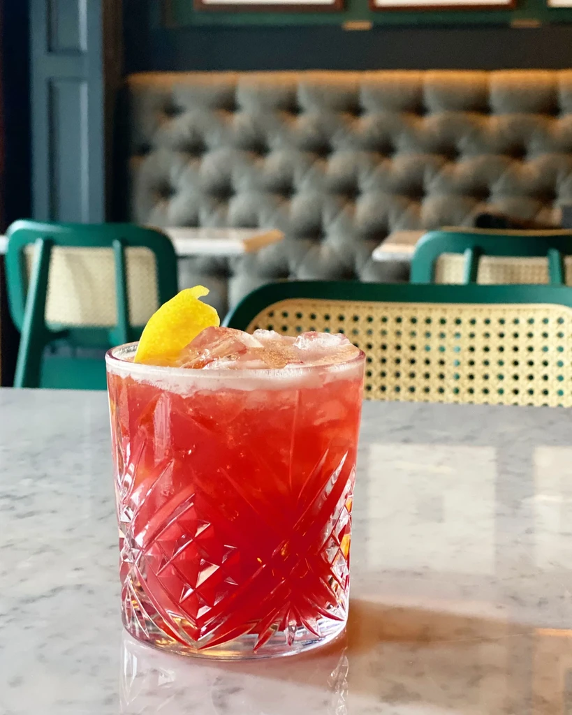 Red cocktail with lemon garnish on a marble table in a restaurant.