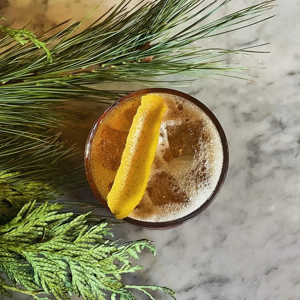 An overhead view of a drink with ice and lemon peel next to pine needles.