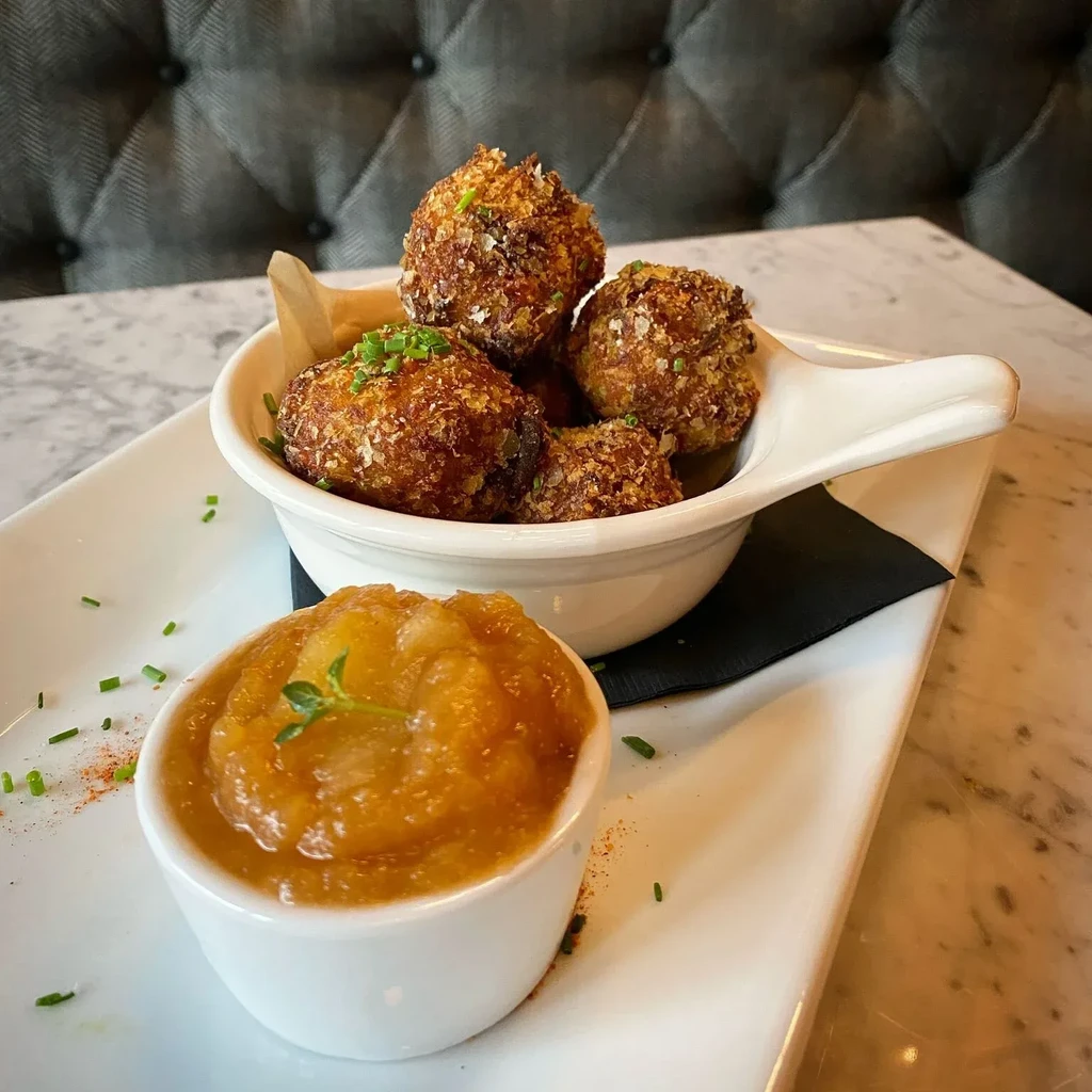 Deep-fried croquettes in a bowl with applesauce on a white plate.