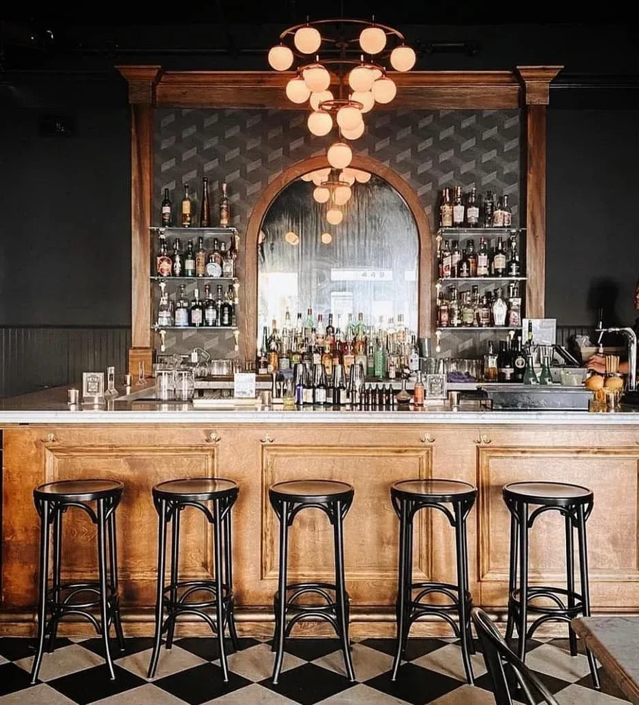 A classic bar with dark wooden accents, bottles, and four stools.