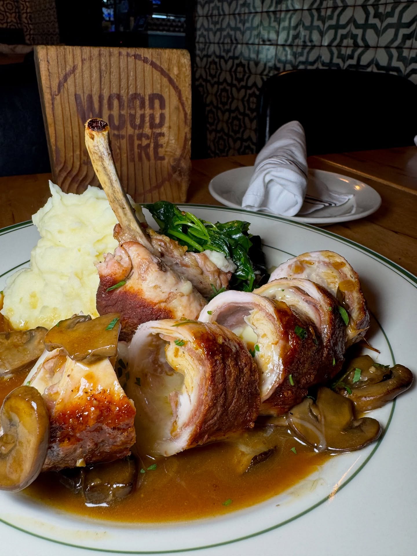 Plate with rolled meat, bone-in meat, mashed potatoes, greens, and mushrooms.