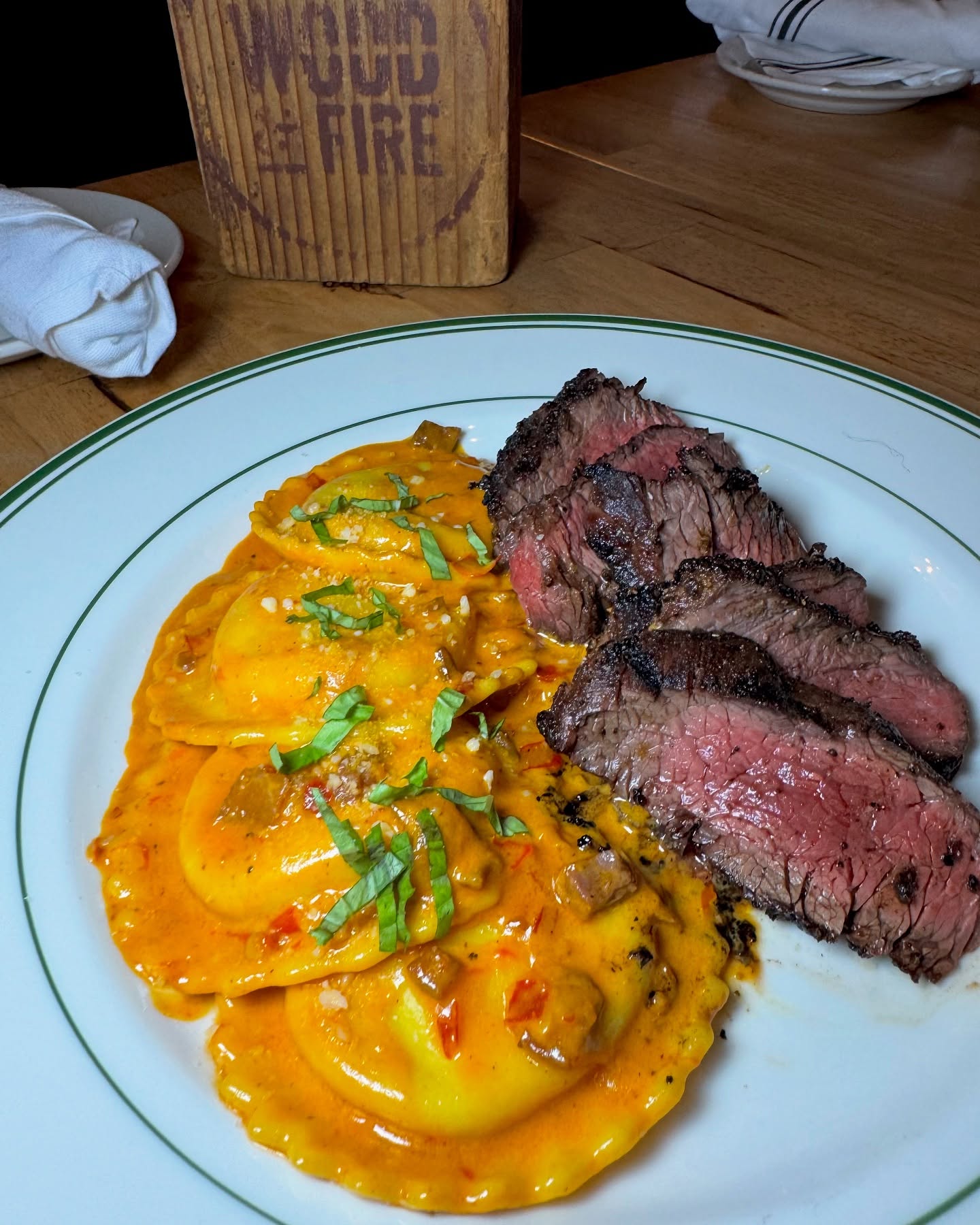 Sliced steak and ravioli in orange sauce, garnished with basil.