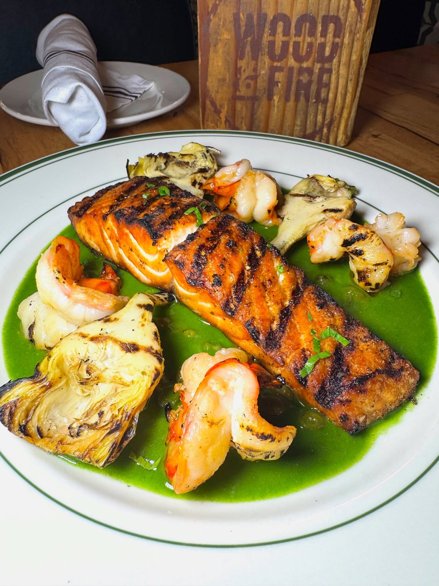 Grilled salmon, shrimp, and artichokes on a white plate with green sauce.
