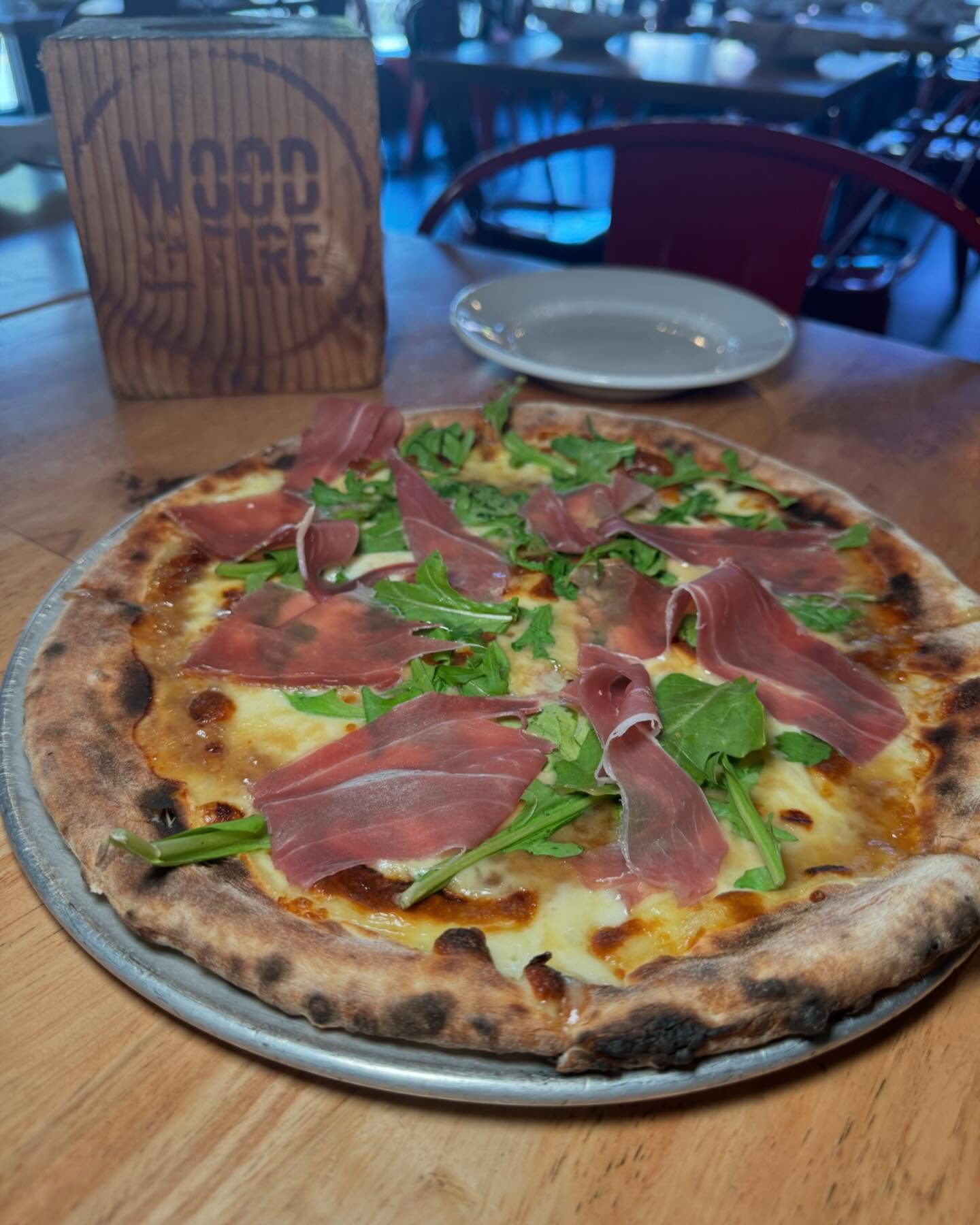 Pizza with prosciutto and arugula, with a 'Wood & Fire' sign.
