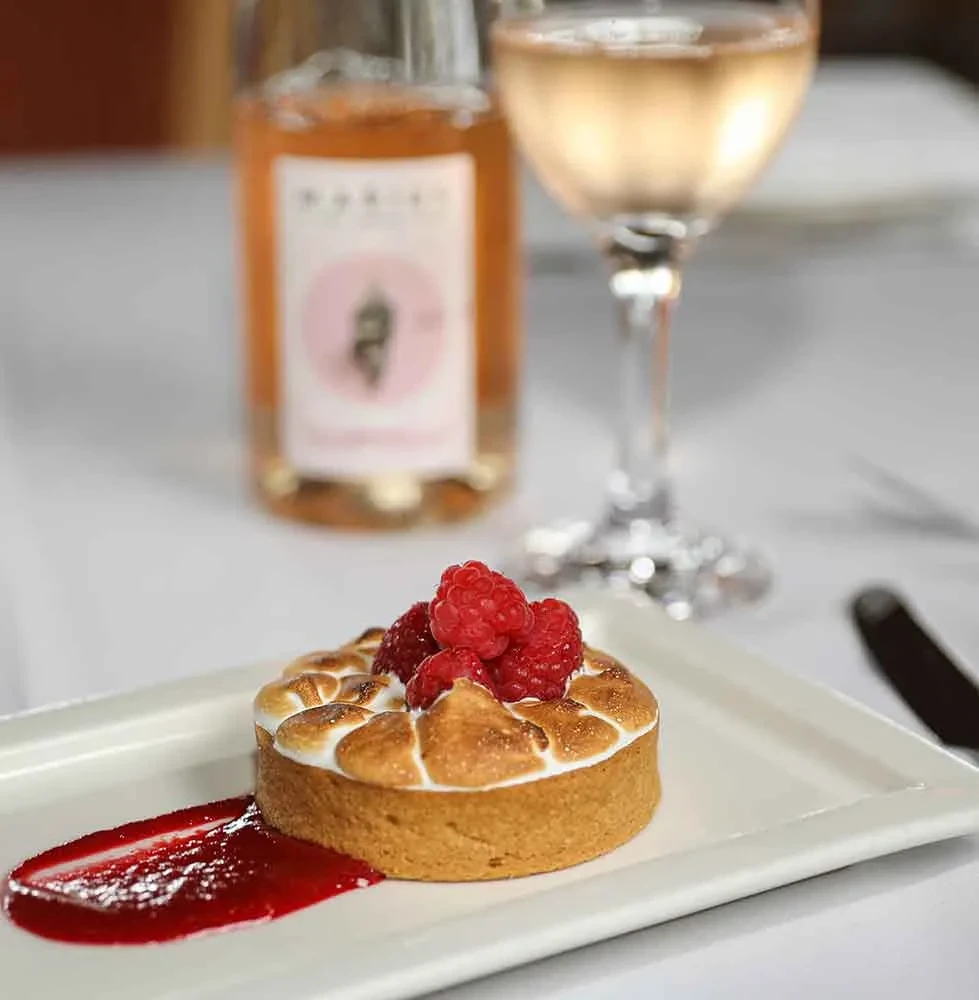 Raspberry meringue tart with berry sauce, a wine glass, and bottle.