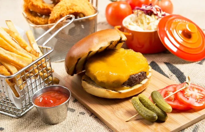 A cheeseburger, fries, onion rings, coleslaw, ketchup, pickles and tomatoes.