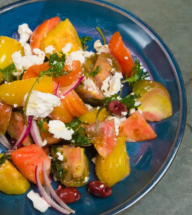 A colorful tomato and feta salad with olives and red onion.