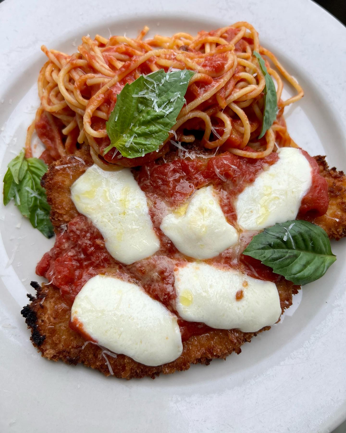 Golden-brown cutlet topped with mozzarella, tomato sauce, spaghetti, and basil.
