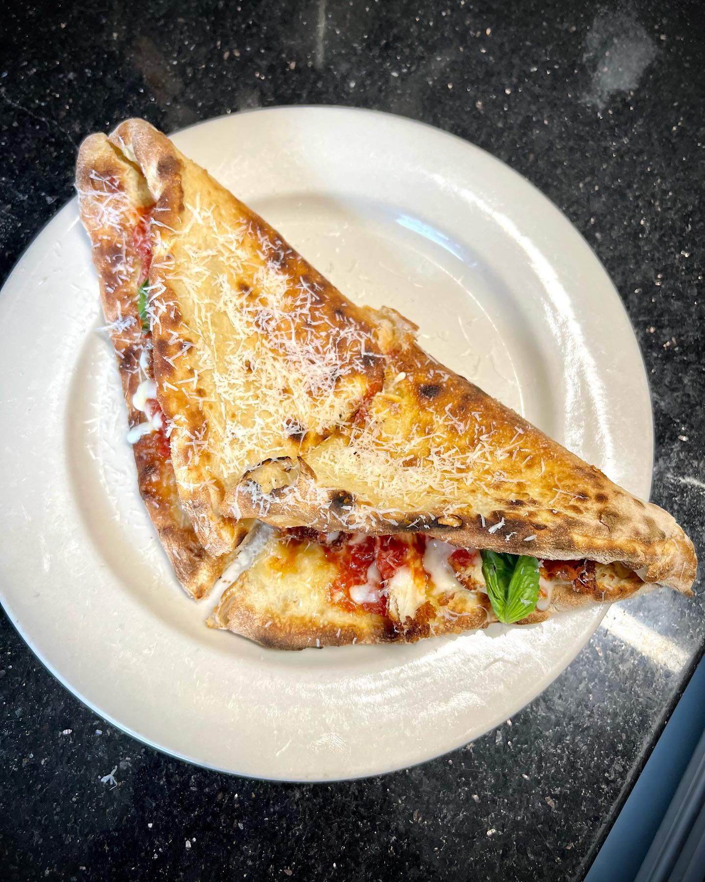 Baked folded pizza with melted cheese, sauce, and basil on white plate.