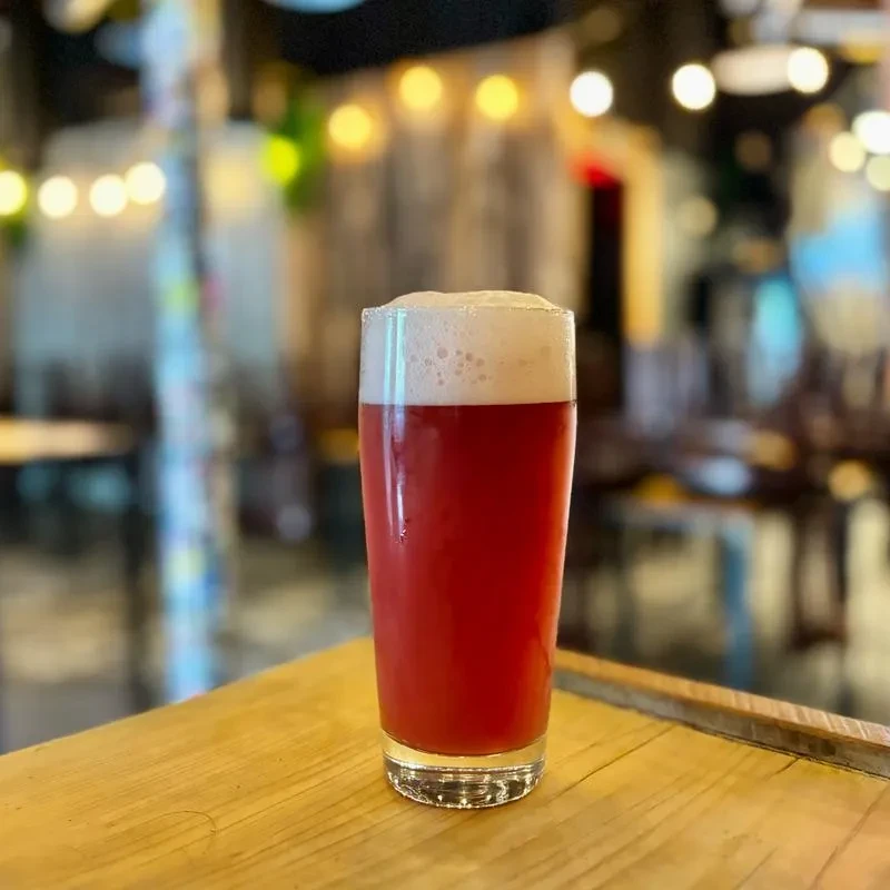 A tall glass of red beer with foam on a wooden table.