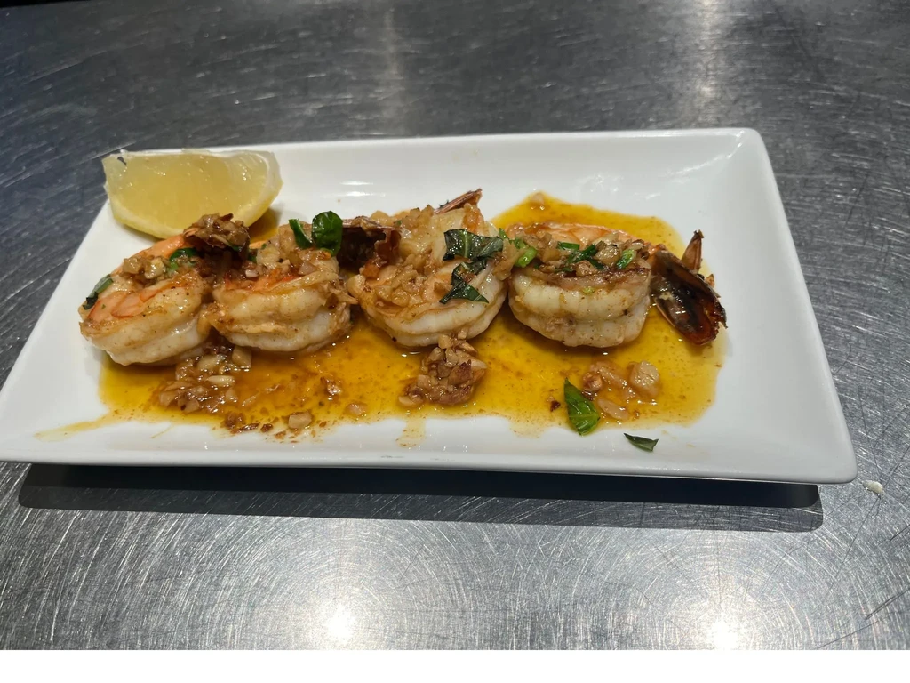 Shrimp scampi with lemon and herbs on a white plate.
