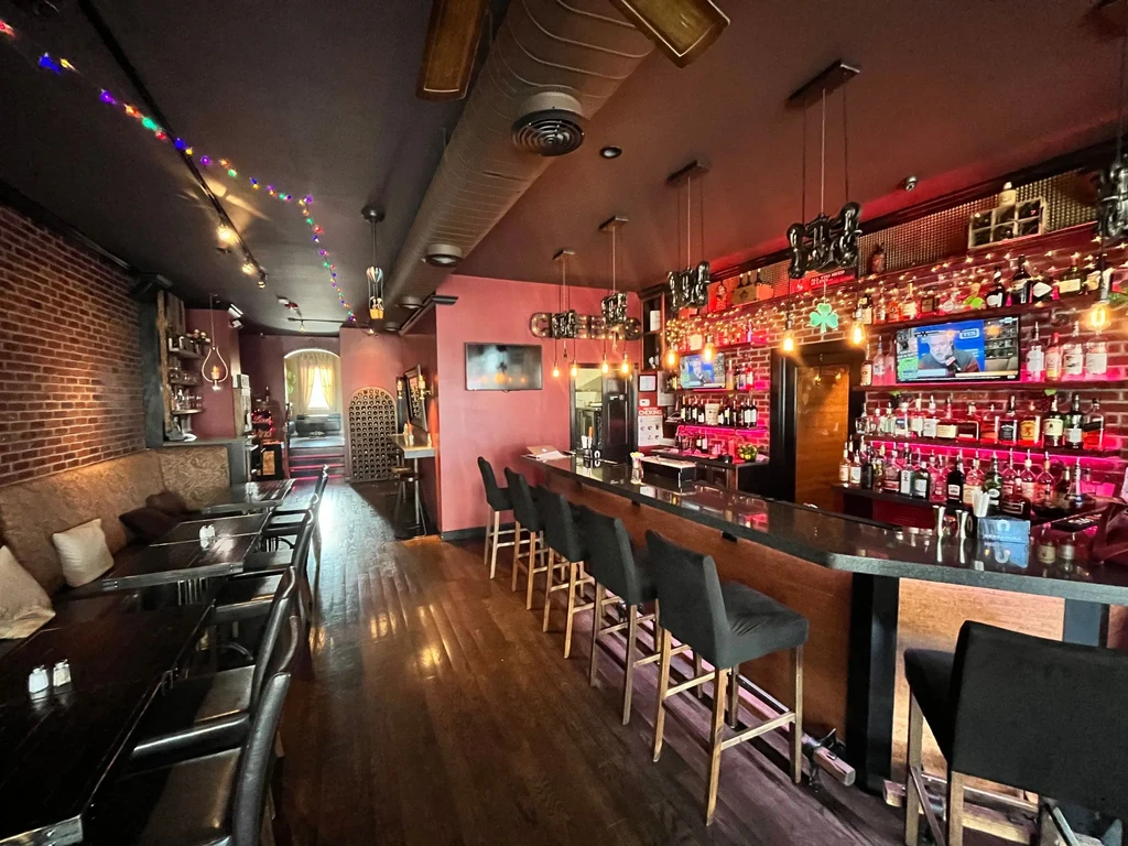 An empty bar and restaurant with brick walls and pink lighting.