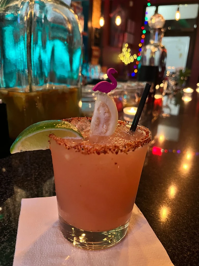 A close-up of a pink cocktail with fruit and a flamingo pick.