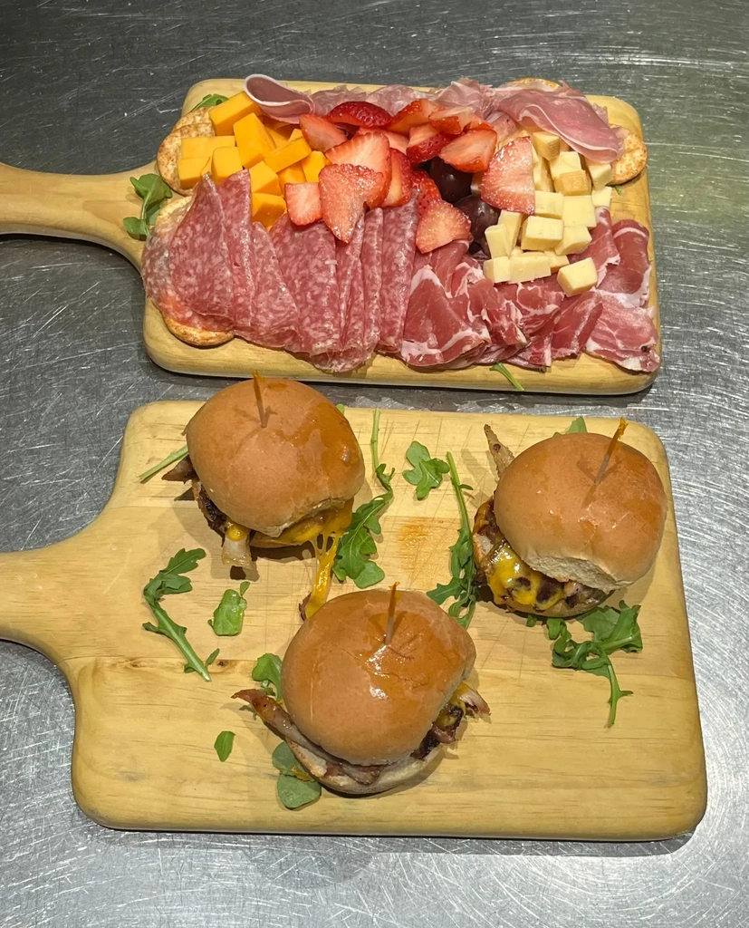 Charcuterie board with cheeses, meats, strawberries and three sliders with arugula.