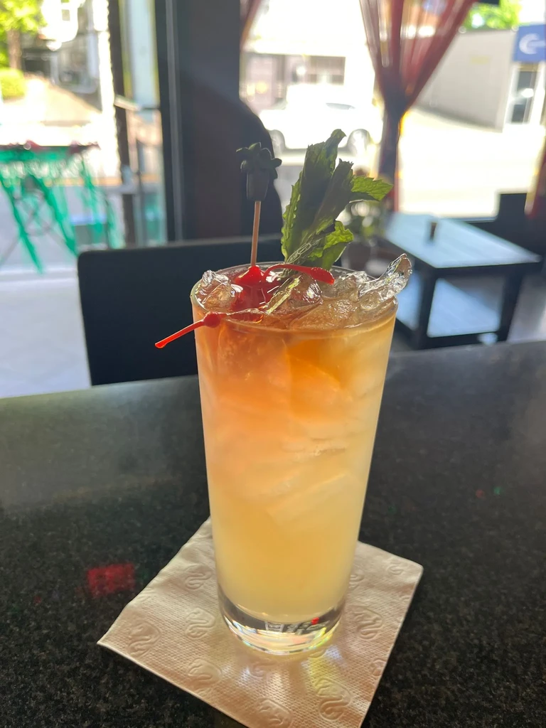 Tall drink with cherries, mint, and ice on a bar counter.