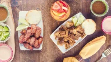Two platters of fried meat, corn cakes, sauces, and drinks on a table.
