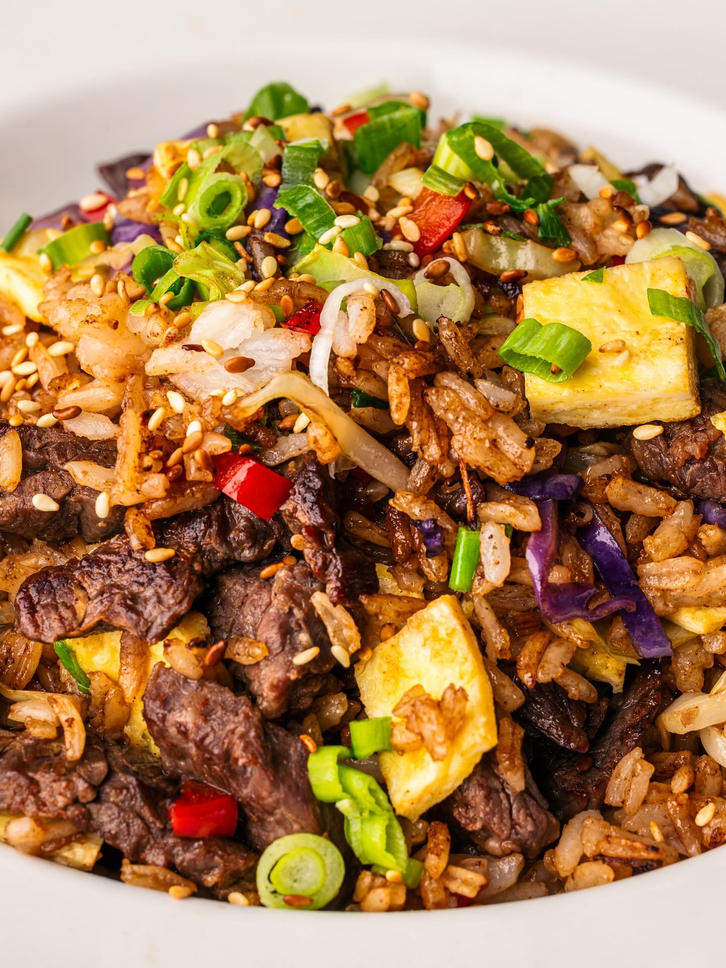 Close-up of beef fried rice with egg, vegetables, and sesame seeds.