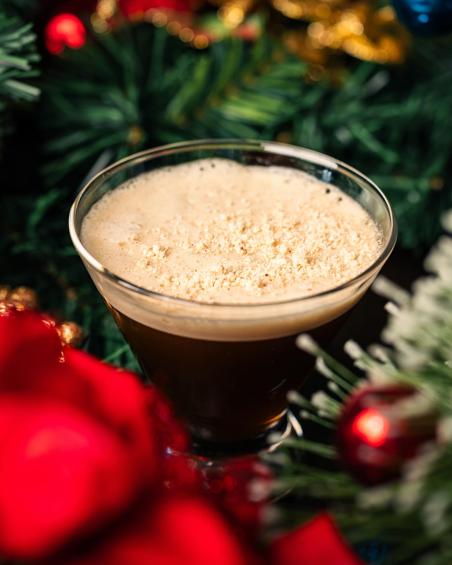 Dark drink with foamy top and sprinkles, surrounded by Christmas decorations.