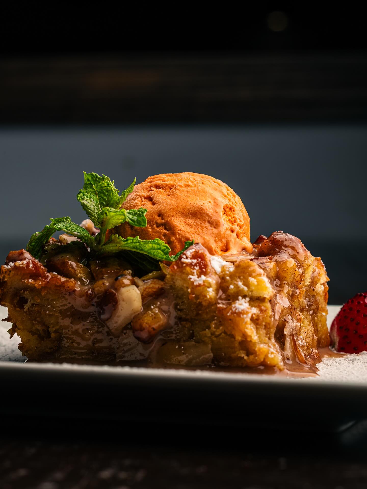 Bread pudding topped with orange ice cream, mint, and strawberry.