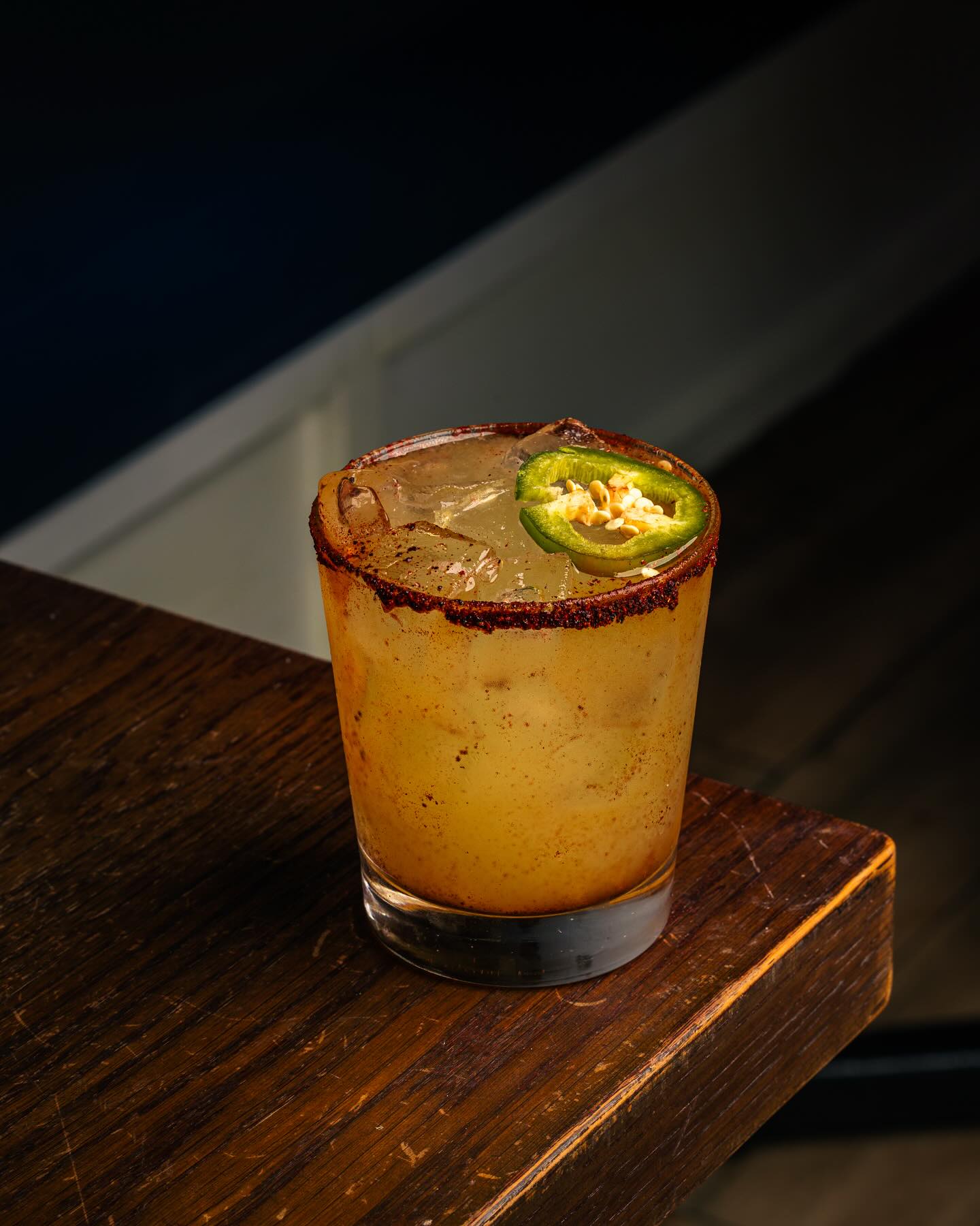 Spiced drink with jalapeño garnish on a wooden table.