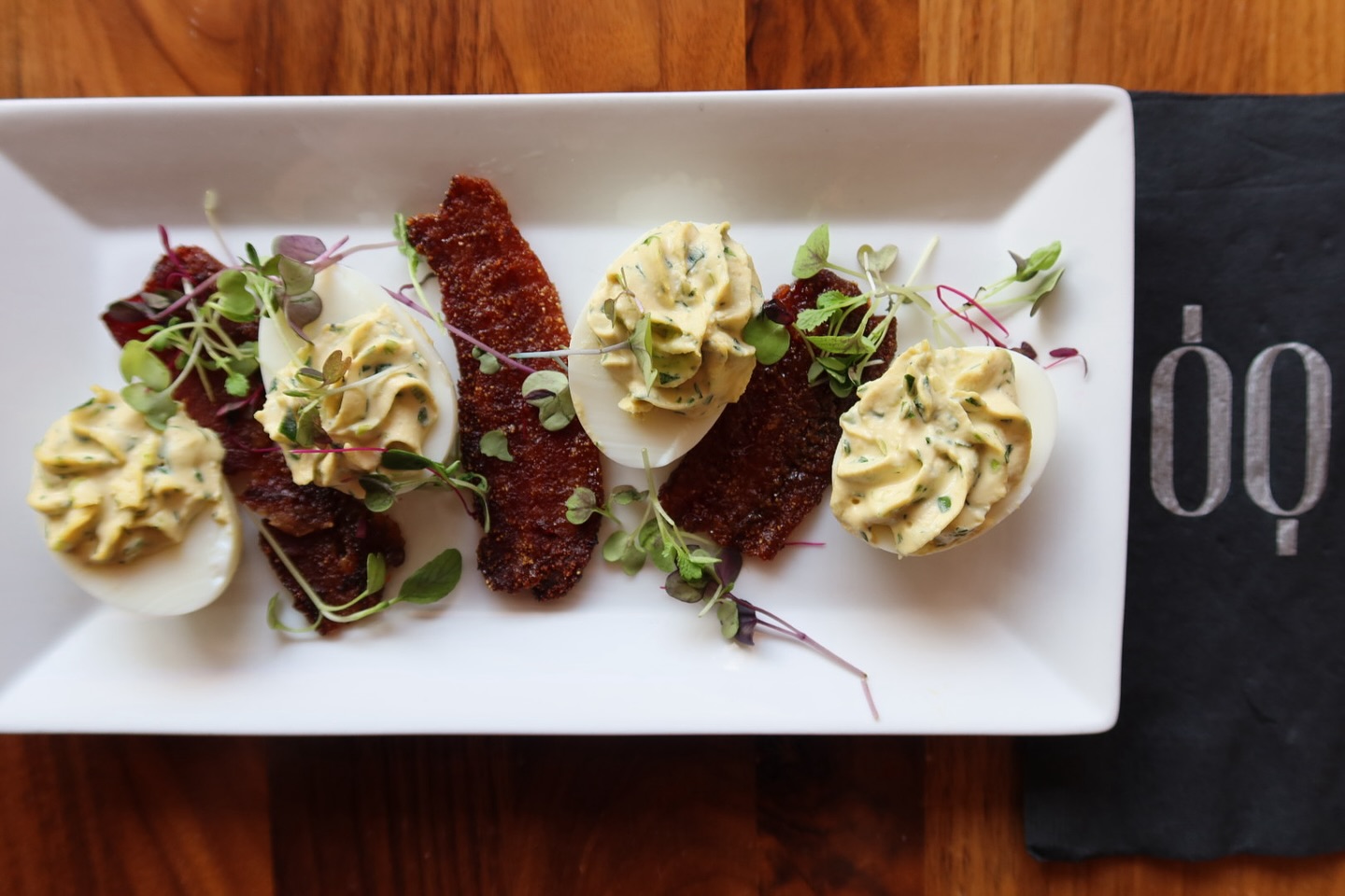 Deviled eggs with crispy bacon and microgreens on a white plate.