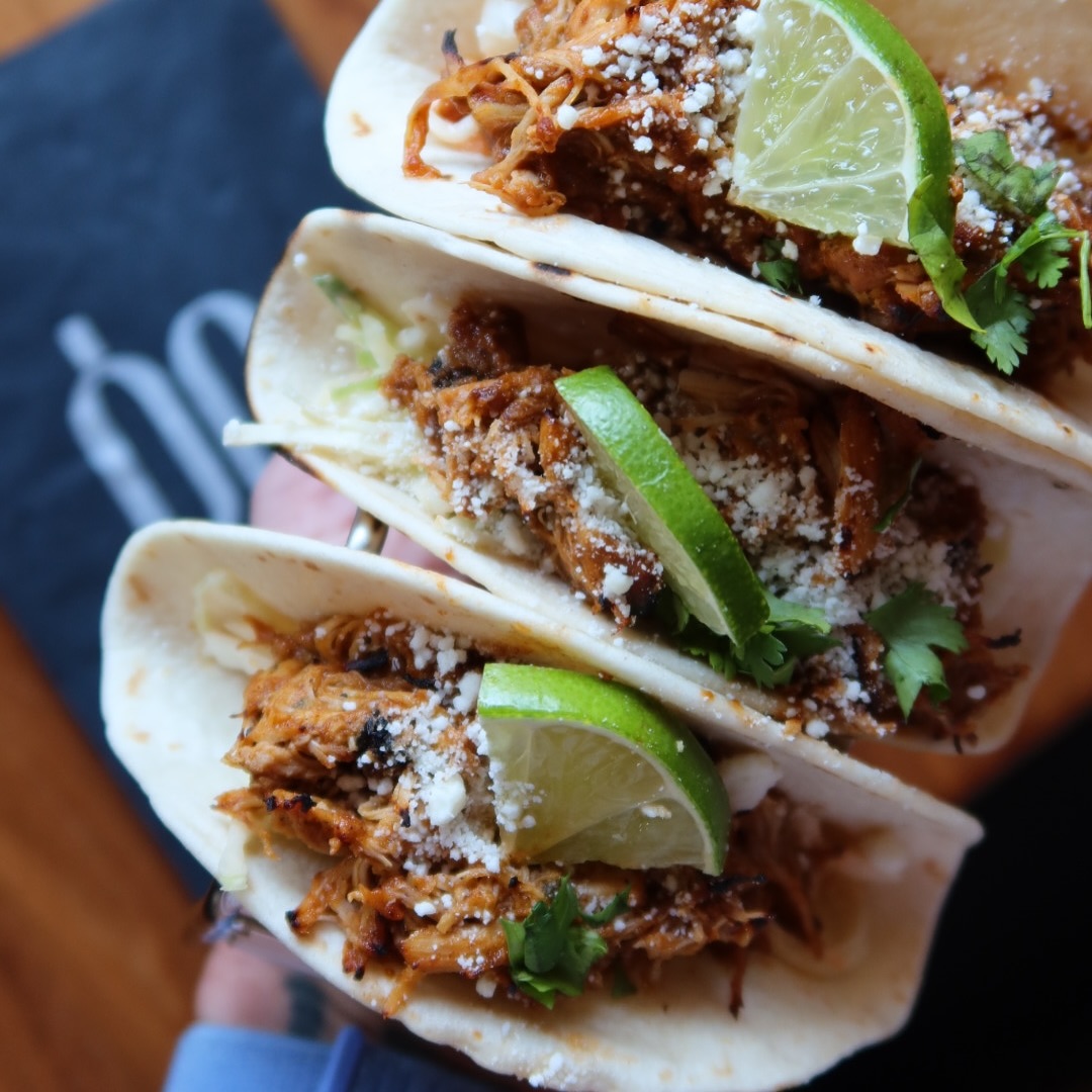 Three soft tacos with shredded meat, cheese, cilantro, and lime.