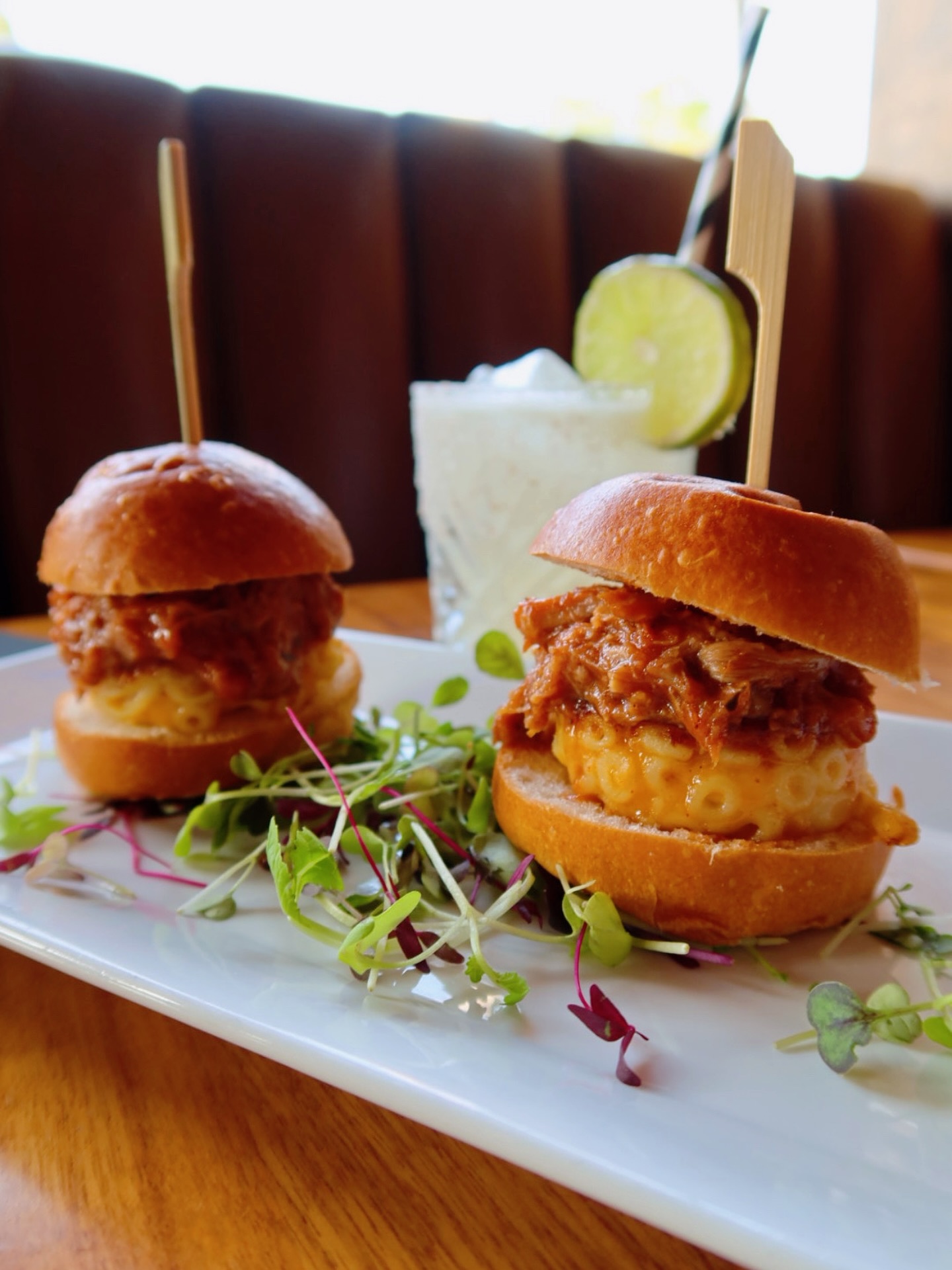 Two sliders with pulled pork, macaroni and cheese, and microgreens.