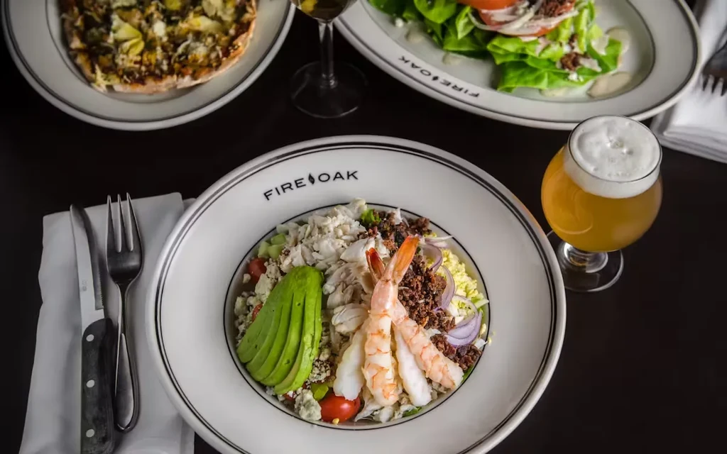 Three dishes and a beer on a dark table at Fire Oak restaurant.