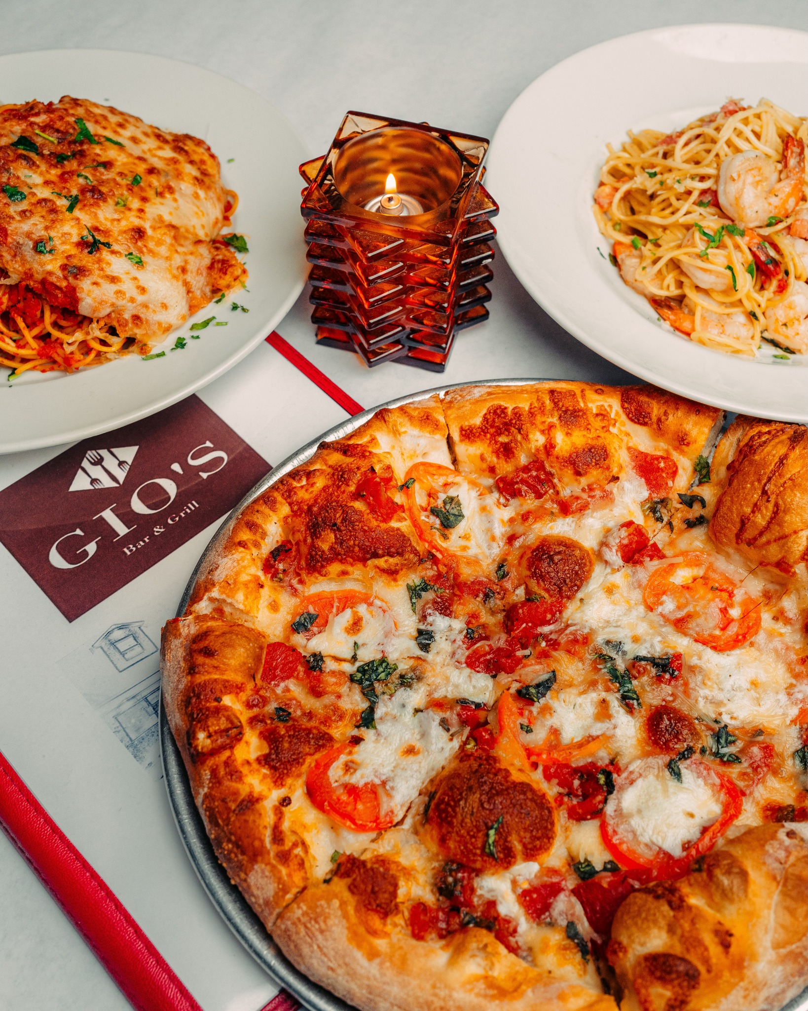 Pizza, pasta dishes, and a lit candle on a table at Gio's.