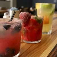 Three glasses of colorful fruit drinks on a wooden bar.