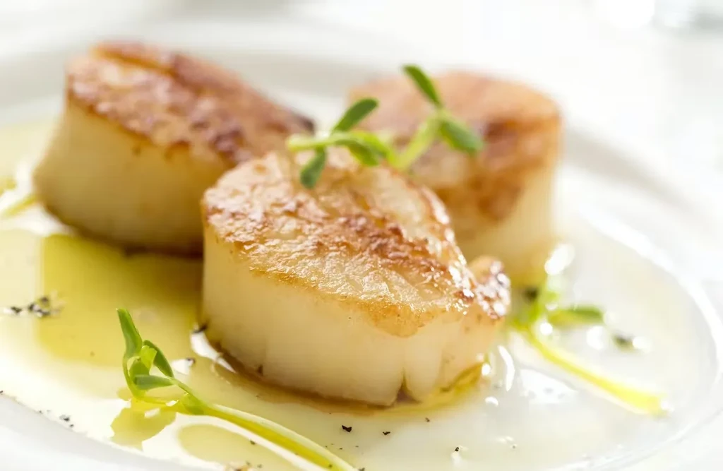 Three seared scallops in a light sauce, garnished with herbs.