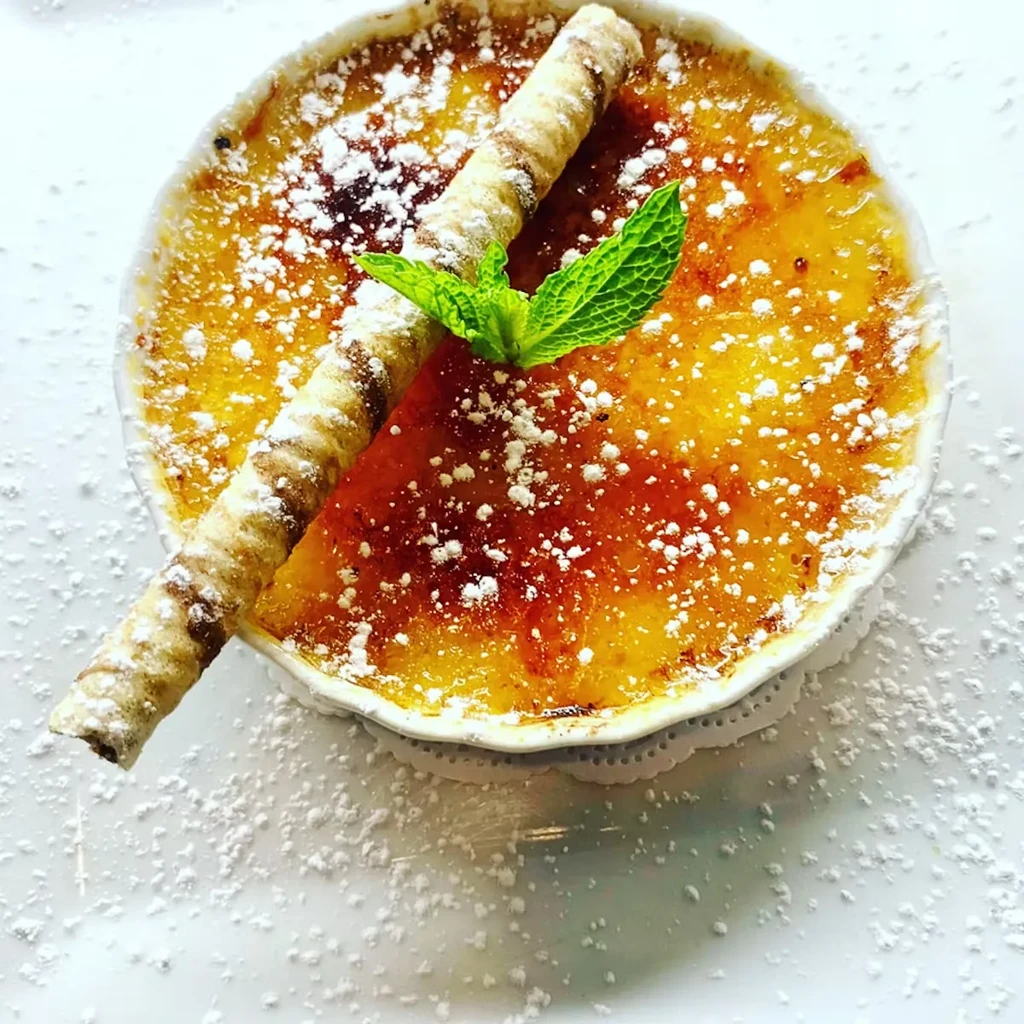 Creme brulee with powdered sugar, wafer roll, and mint leaf.