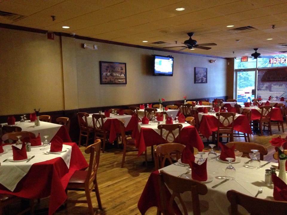 Warmly lit restaurant interior with tables set with red and white linens.